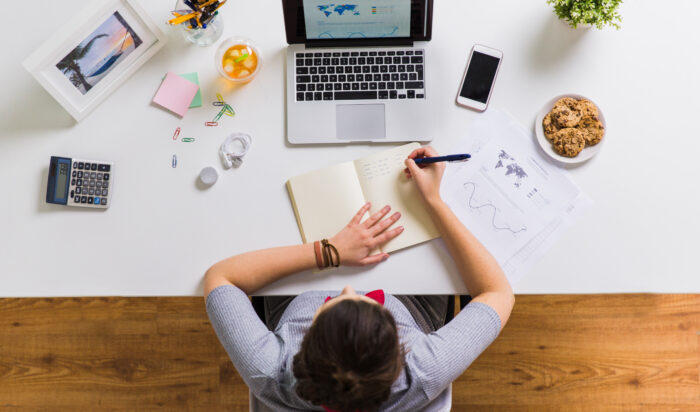 woman with laptop writing to notebook at office business, freelance and people concept - woman with laptop computer writing to notebook at office